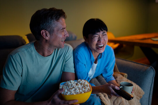 Couple laughing watching comedy show eating popcorn at home
