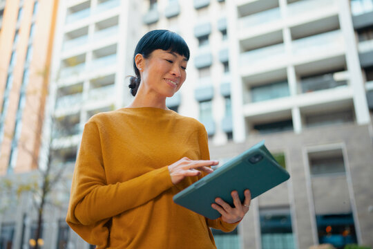 Asian woman using tablet outdoors in urban setting
