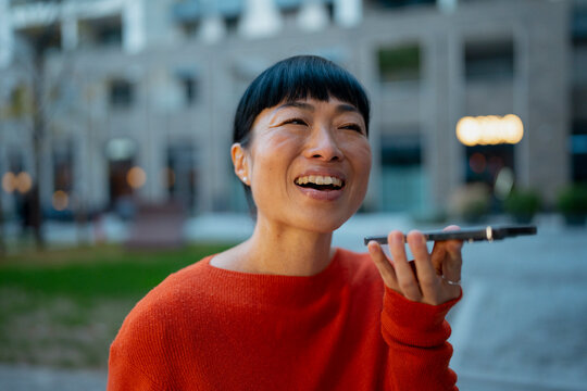 Asian woman sending voice message with smartphone outdoors
