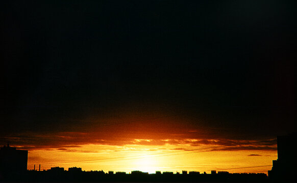 Golden sunset sky glowing over dark city skyline silhouette at dusk.