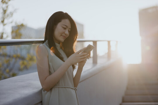 Young Woman Using Smartphone at Sunset Outdoors With a Smile