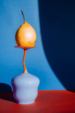 Orange pear balanced on a colorful vase