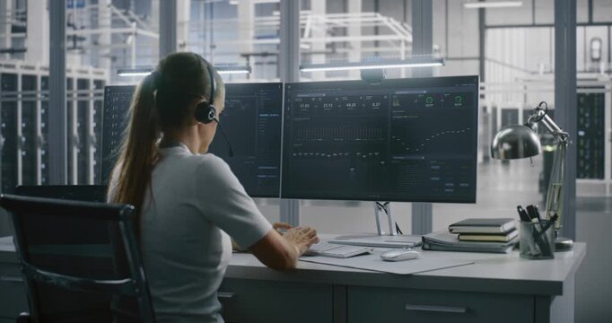 Female Technical Specialist Communicates Via Headset While Tracking Metrics and Graphs Data on Multi Screen Setup in Data Center. Control and Support, Expert Consultation, and Complex Problem Solving.