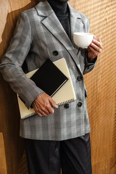 Business person in grey blazer holding coffee and notebooks