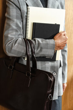 Person holding notebooks and leather bag in business outfit