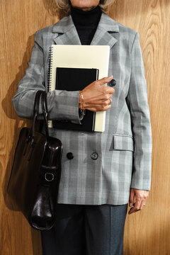 Businessperson holding notebooks and leather bag in front of wood wall