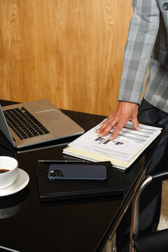 Hand leaning on desk with financial report, laptop and phone