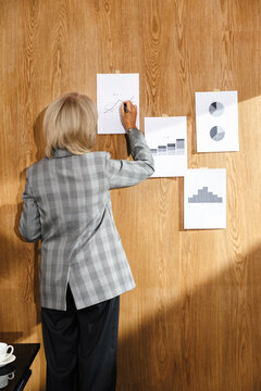 Businesswoman analyzing printed charts on wooden wall