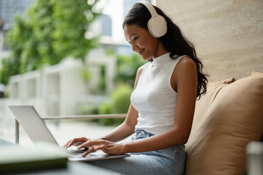 Young Woman Working on Laptop Outdoors with Headphones at Cafe