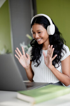Smiling Woman with Headphones Waving at Laptop During a Virtual Call