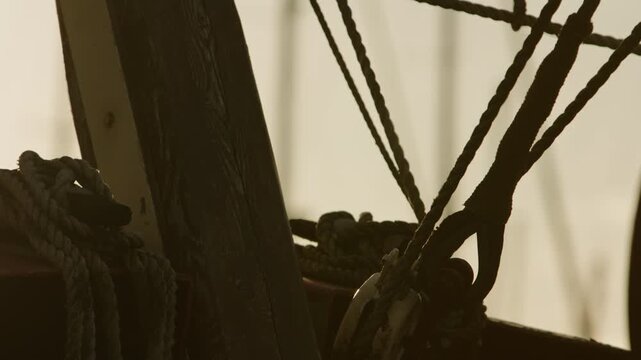 Backlit close-up of nautical ropes and a wooden mast on a traditional boat, creating a warm maritime atmosphere and symbolizing craftsmanship, connection and calmness.
