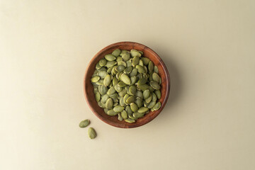 Green Pumpkin seeds in a wooden bowl placed on a beige background.