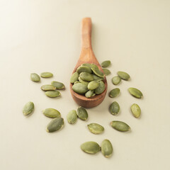 Green Pumpkin seeds in a wooden spoon placed on a beige background.