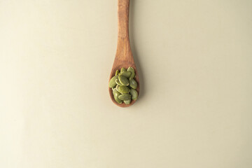Green Pumpkin seeds in a wooden spoon placed on a beige background.