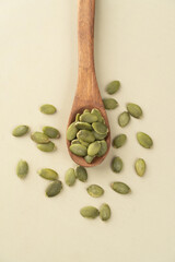 Green Pumpkin seeds in a wooden spoon placed on a beige background.