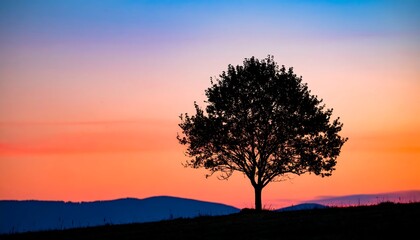 A solitary tree silhouette stands against a vibrant sky of orange, pink, and blue hues over distant hills at dusk