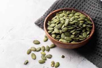 Green Pumpkin seeds in a wooden bowl placed on a textured background.