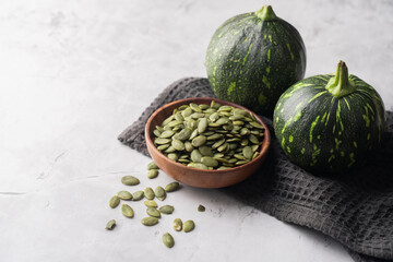 Green Pumpkin seeds in a wooden bowl, along with green baby pumpkin, placed on a textured background.