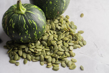 Green Pumpkin seeds, along with a baby pumpkin, placed on a textured background.