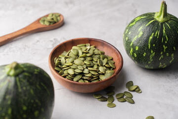 Green Pumpkin seeds in a wooden bowl, along with green baby pumpkin, placed on a textured background.