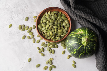 Green Pumpkin seeds in a wooden bowl, along with green baby pumpkin, placed on a textured background.