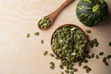 Green Pumpkin seeds in a wooden bowl, along with green baby pumpkin, placed on a textured background.