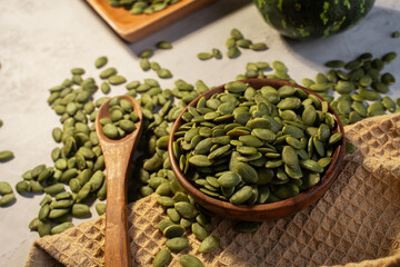 Green Pumpkin seeds in a wooden bowl, along with green baby pumpkin, placed on a textured background.