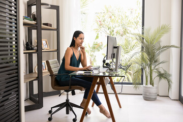 Focused young indigenous freelancer woman working at computer at home, sitting in apartment...