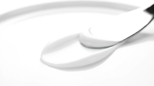 A minimalist close-up of a dollop of white cream on a smooth, white surface, with a utensil