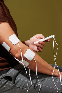 man uing an electrostimulation device with electrodes on his elbow
