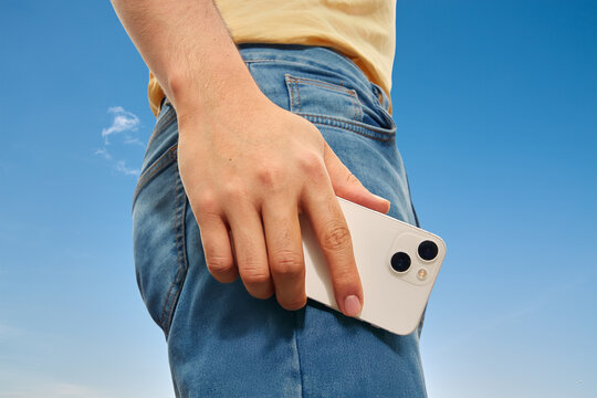 Close-up of hand holding smartphone next to jeans pocket