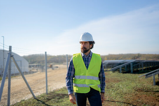 Worker inspects solar farm site in safety gear during bright sunny day
