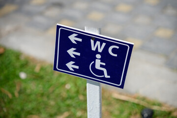 Close-up of sign with arrows pointing to restrooms and accessible areas, outside beach resort. Wheelchair-accessible sign is on blue background.