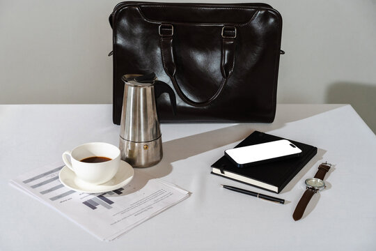 Business accessories, leather briefcase, coffee, phone, and documents