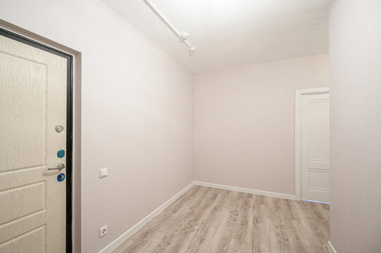minimalist hallway with light beige walls, light wood laminate flooring, white baseboards, two doors (one with security locks), recessed ceiling lights, and neutral decor