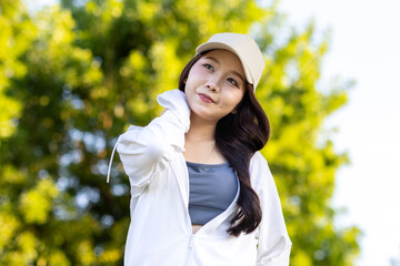 Asian woman wearing wireless headphones, smiling while relaxing in a park after workout and stretching, enjoying music and peaceful outdoor moment of contentment and well-being.
