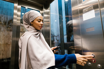 Muslim woman pressing elevator button using smartphone