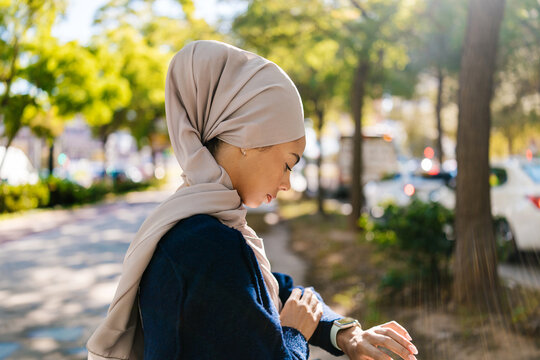 Muslim woman checking time on smartwatch in urban park