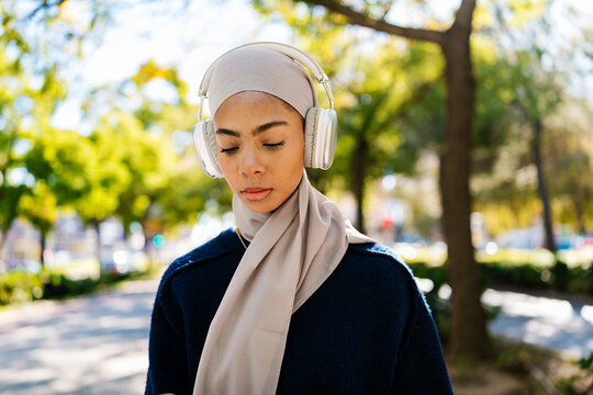 Muslim woman wearing hijab and headphones listening music outdoors