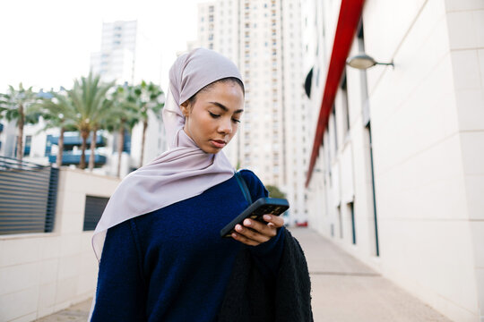 Muslim woman wearing hijab texting on a smartphone walking