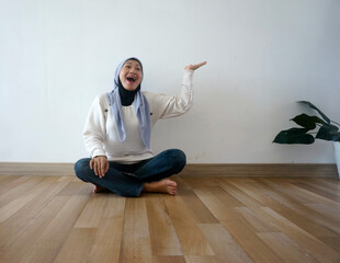 Fototapeta premium Joyful Muslim Woman in Hijab Gesturing Upwards on Wooden Floor