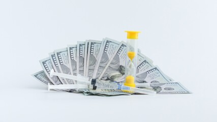 Time and Money Hundred Dollar Bills with Hourglass and Syringe on White Background. Concept