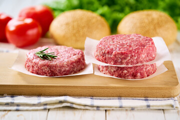 Raw ground beef burger patties separated by parchment paper on a white table, selective focus.