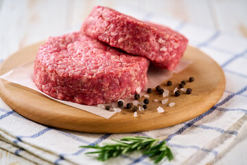Two raw beef burger patties with peppers and salt on a white table. Ideal ingredient for grill, BBQ .