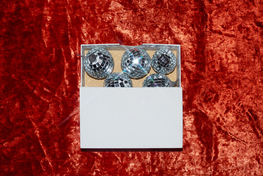 Shiny ornaments stored in a white box on a plush red background