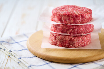 Stack of raw beef burger patties separated by parchment paper on a  white wooden table and copy space for text.