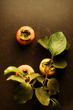Fresh ripe persimmons with green leaves on black rustic background