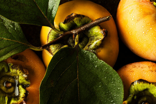 Fresh ripe persimmons with green leaves, close up full frame