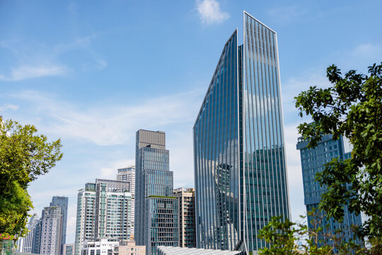 Skyscrapers rise against a blue sky, framed by greenery.