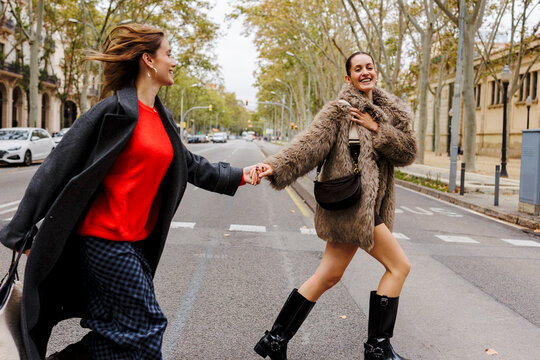Happy female friends holding hands crossing street
